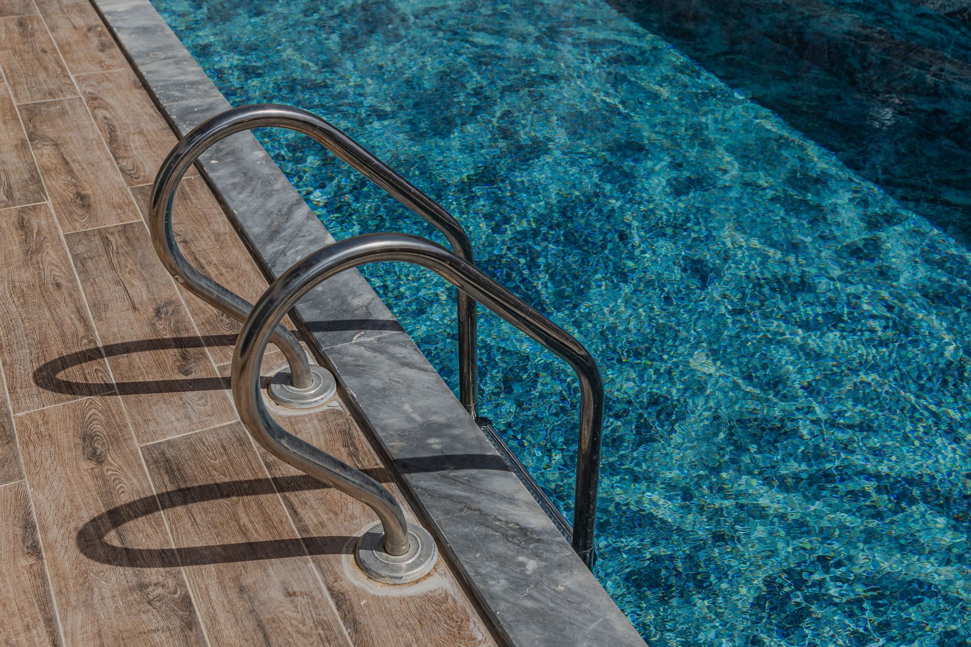 Close-up of pool ladder by clear blue water, capturing summer vibes.