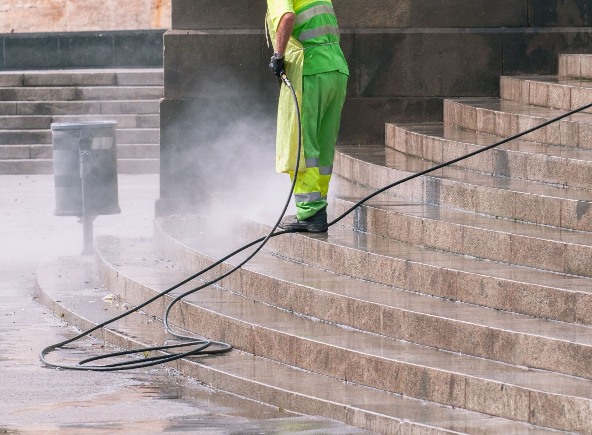 A street worker pressure washes stone stairs in a public park, ensuring cleanliness and safety.