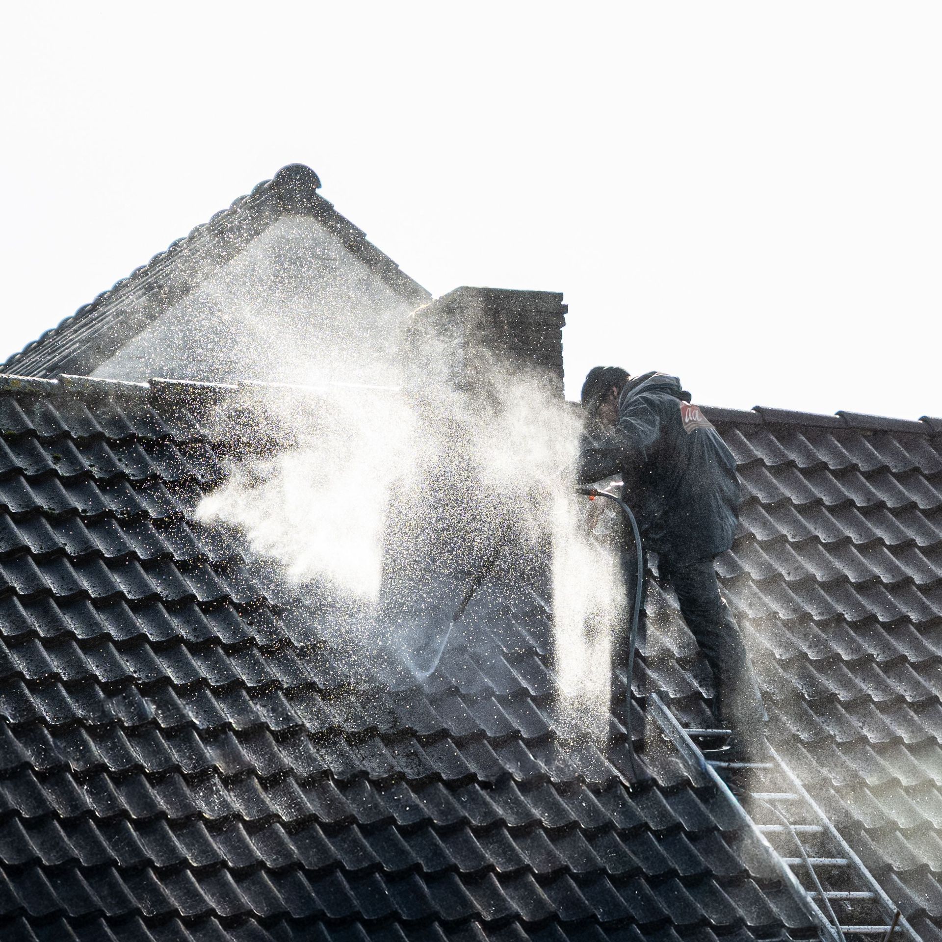 Worker power washing roof tiles, removing grime and buildup.